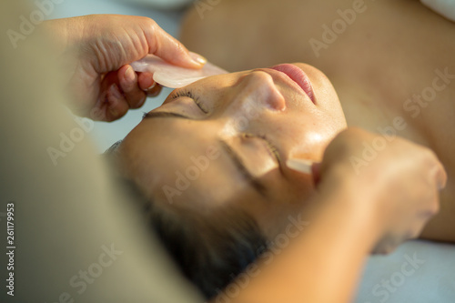 Young woman receives facial rejuvenation with gua sha rose quartz in spa wellness center photo