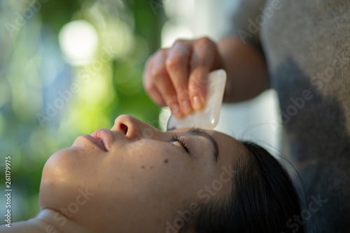 Young woman receives facial rejuvenation with gua sha rose quartz in spa wellness center