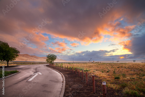 A sunset forming over a wet one way road after a rain storm