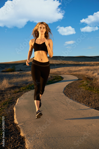 A young woman in black active wear jogging on an outdoor running trail on a Fall Afternoon.