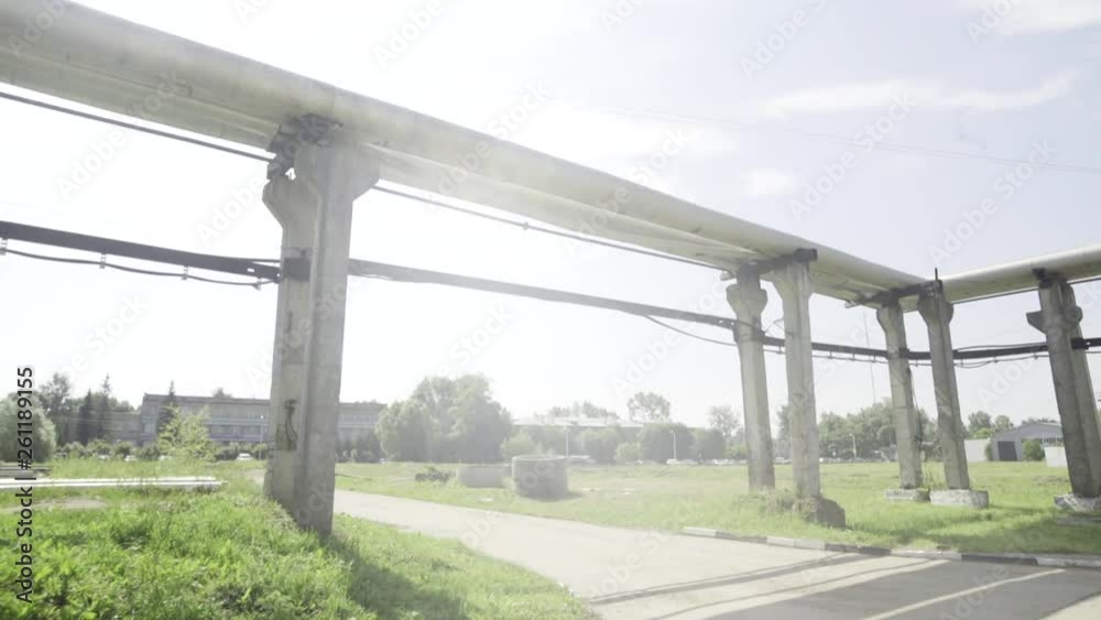 Industrial metal pipelines are laying outside and around large plant building territory above ground and grass lawn on sunny warm summer day. Industrial metal pipelines are laying outside and around large plant building territory above ground and grass lawn on sunny warm summer day.