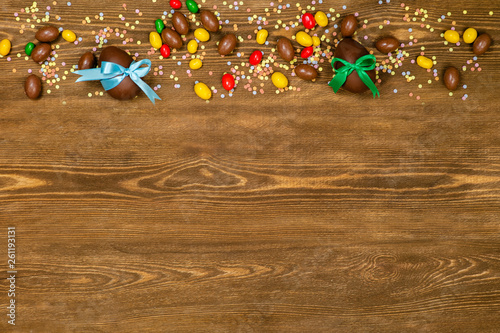 Chocolate Easter eggs and sweets over brown wooden background. Empty space foe text