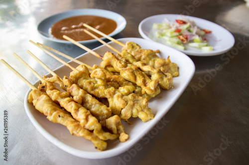 Pork satay skewers on the white dish with salad and sauce on the metal table. Asian cuisine