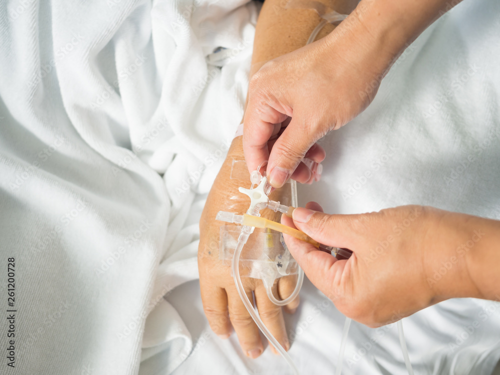 Obraz premium Close up nurse hand adjust set iv fluid intravenous drop saline drip in hospital room with blurry patient woman on hospital bed.Medical treatment emergency patient.Caregiver and hopeful concept.