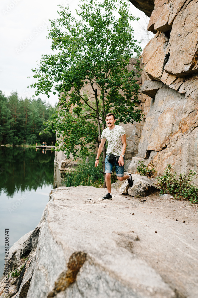 A man run on background of the large rocks wall on a big stone. full length, view from down side. looking at the camera. Close up. Place for text and design. Man poses at cliff near lake.