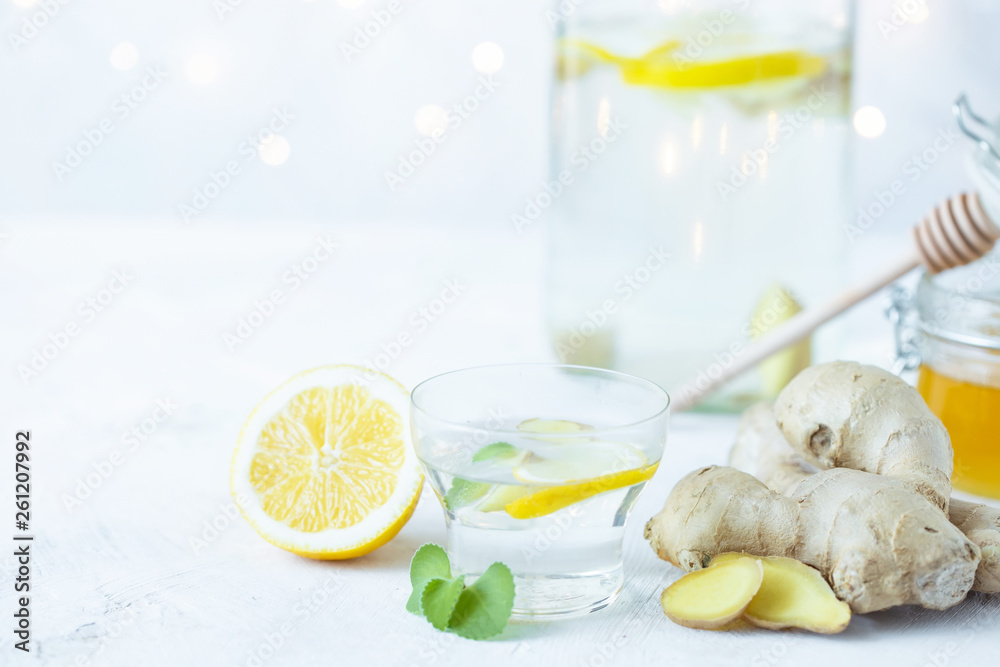 Healthy ginger drink in a cup. Ginger root, honey in a jar, lemon on a white table.