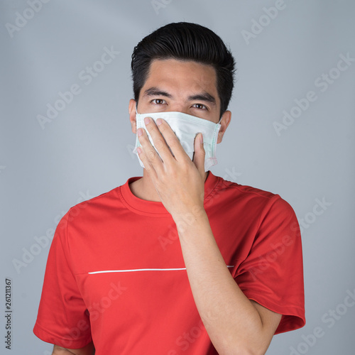 Sick young man handsome and sneeze wearing medical mask and red shirt isolated on gray wall background. Concept of sick. Asia people.