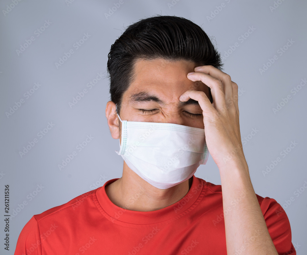 Sick young man handsome and headache wearing medical mask and red shirt isolated on gray wall background. Concept of headache. Asia people. Sick young man handsome and headache wearing medical mask and red shirt isolated on gray wall background. Concept of headache. Asia people.