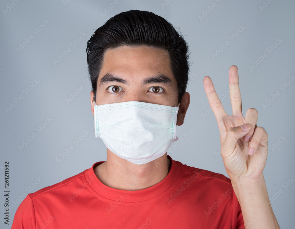 Sick young man wearing medical mask and red shirt come on sign isolated on gray wall background. Concept of headache. Asia people. Sick young man wearing medical mask and red shirt come on sign isolated on gray wall background. Concept of headache. Asia people.