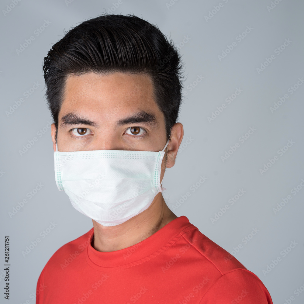 Sick young man handsome and sneeze wearing medical mask and red shirt isolated on gray wall background. Concept of sick. Asia people.