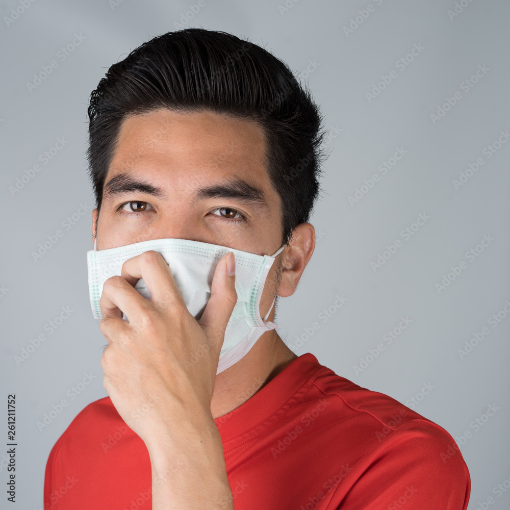 Sick young man handsome and sneeze wearing medical mask and red shirt isolated on gray wall background. Concept of sick. Asia people. Sick young man handsome and sneeze wearing medical mask and red shirt isolated on gray wall background. Concept of sick. Asia people.