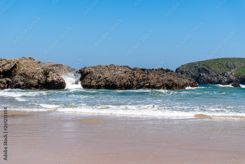 Scenic view of sand beach with rocks against blue sky