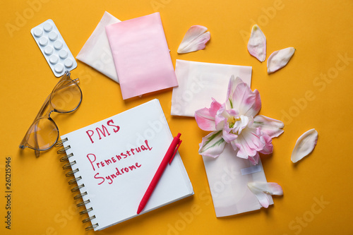 Composition with menstrual pads, notebook with text PMS, PREMENSTRUAL SYNDROME, flower and pills on color background photo