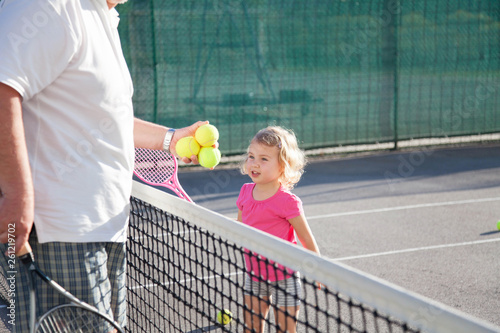 Kid is playing tennis on court. Cute child has workout with teacher or trainer. Sports activities outdoors in summer. Little girl is having fun. photo