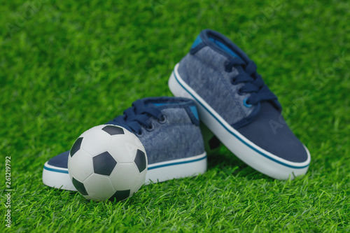 Concept encourage children to play sport  exercise for a healthy body  shoes of small baby shoes next to ball isolated on grass background.
