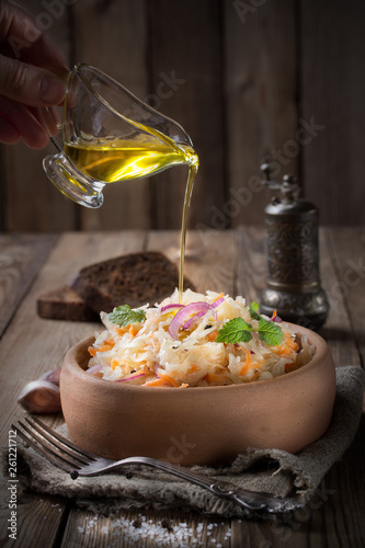 Sauerkraut with onions and mint, in a pottery,pour olive oil. Pieces of black rye bread and a pepper shaker on the back of a wooden background.