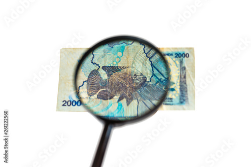 Two thousand Ugandan shillings bill and magnifying glass isolated on white background