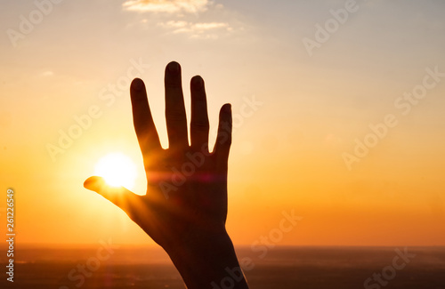 the hand reaches for the sky and closes the sun, the sun's rays pass through the hand, close-up