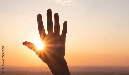 the hand reaches for the sky and closes the sun, the sun's rays pass through the hand, close-up