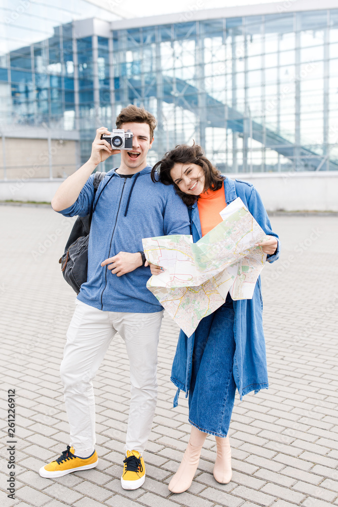 Young cute couple - a boy and a girl walking around the city with a map and camera in their hands. Young people travel.