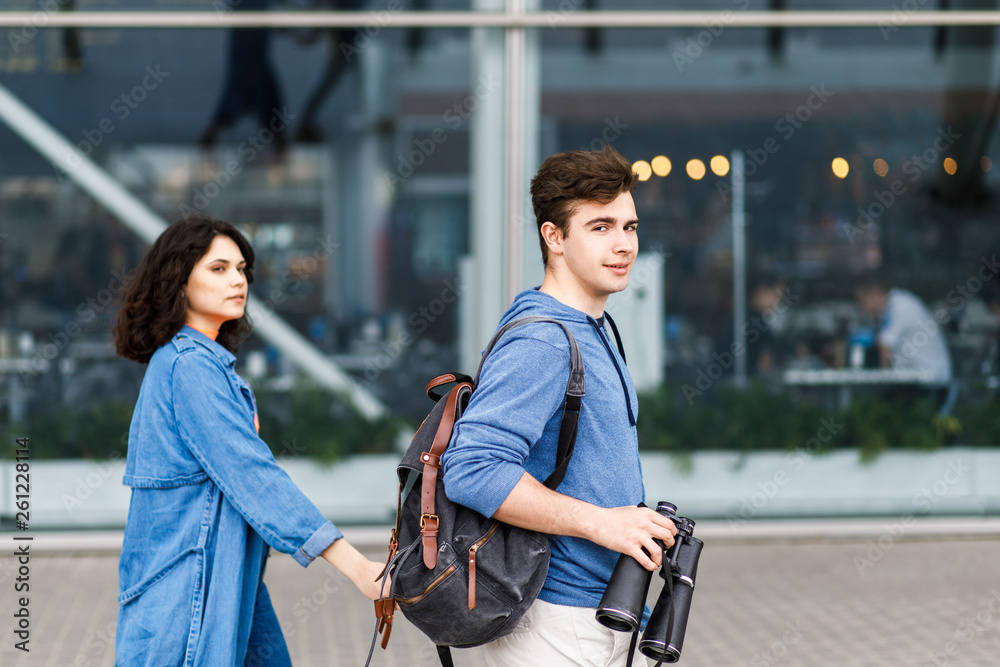 Young pretty couple - a boy and a girl walking around the city with a binocular in his hands. Young people travel. Young pretty couple - a boy and a girl walking around the city with a binocular in his hands. Young people travel.
