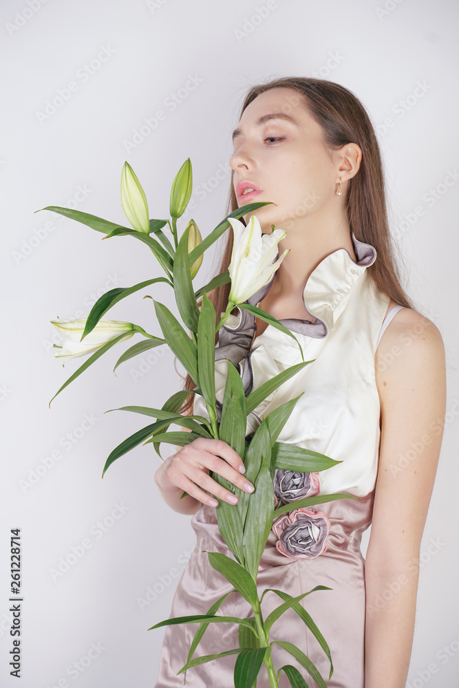 charming young caucasian girl in a pretty dress holds a lush Lily flower in her hands and stands on a white background in the Studio alone charming young caucasian girl in a pretty dress holds a lush Lily flower in her hands and stands on a white background in the Studio alone