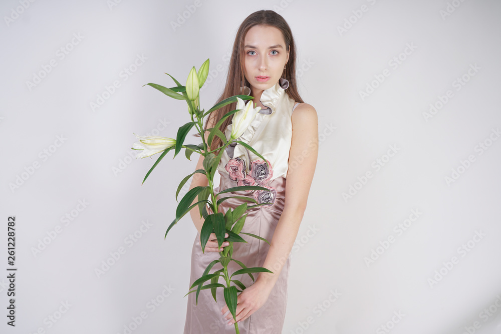 charming young caucasian girl in a pretty dress holds a lush Lily flower in her hands and stands on a white background in the Studio alone charming young caucasian girl in a pretty dress holds a lush Lily flower in her hands and stands on a white background in the Studio alone