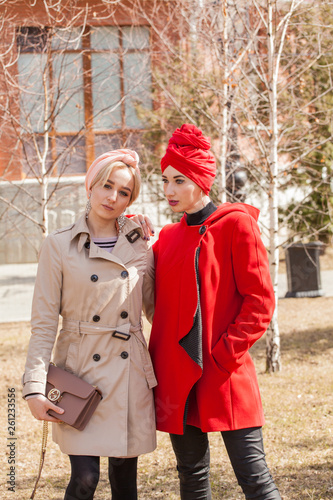 Stylish girls with trendy knitted headscarves. Red turban and pink wrinkle. The image of modern women in the city on the background of architecture