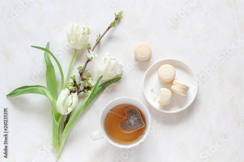 Spring blossoms and a cup of tea with a heart shape tea bag and macaroons on a bright background  flat lay style with a copy space