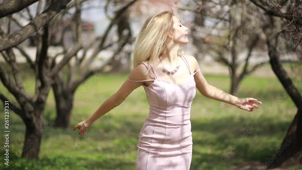 Young woman has fun, enjoys and spinning in the spring garden against the background of apricot trees. Young woman has fun, enjoys and spinning in the spring garden against the background of apricot trees.