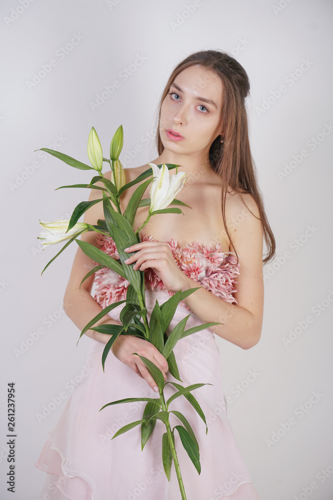 charming young caucasian girl in a pretty dress holds a lush Lily flower in her hands and stands on a white background in the Studio alone charming young caucasian girl in a pretty dress holds a lush Lily flower in her hands and stands on a white background in the Studio alone