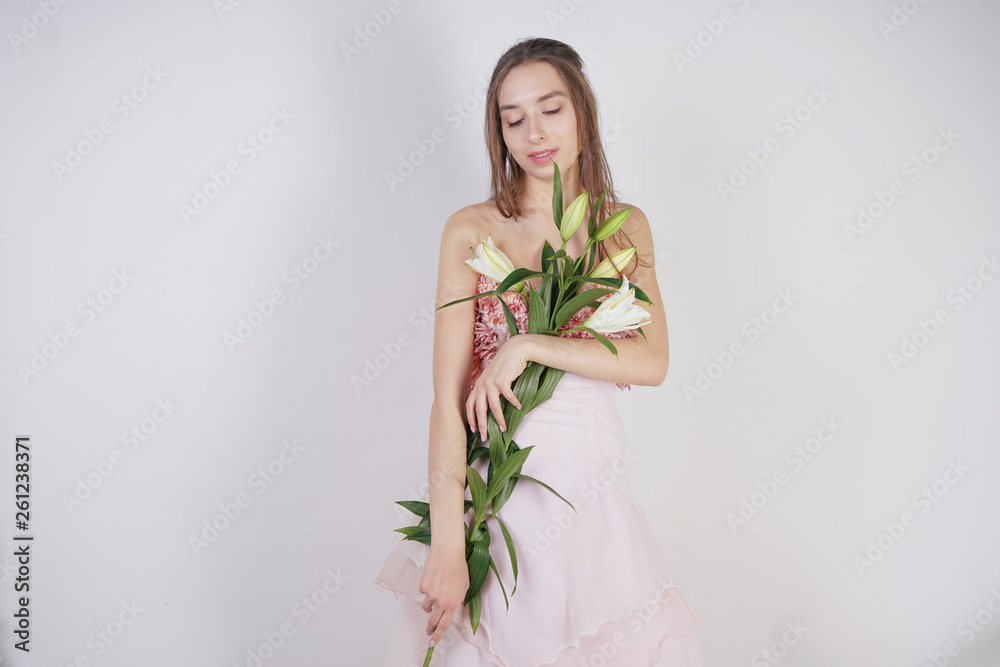charming young caucasian girl in a pretty dress holds a lush Lily flower in her hands and stands on a white background in the Studio alone charming young caucasian girl in a pretty dress holds a lush Lily flower in her hands and stands on a white background in the Studio alone