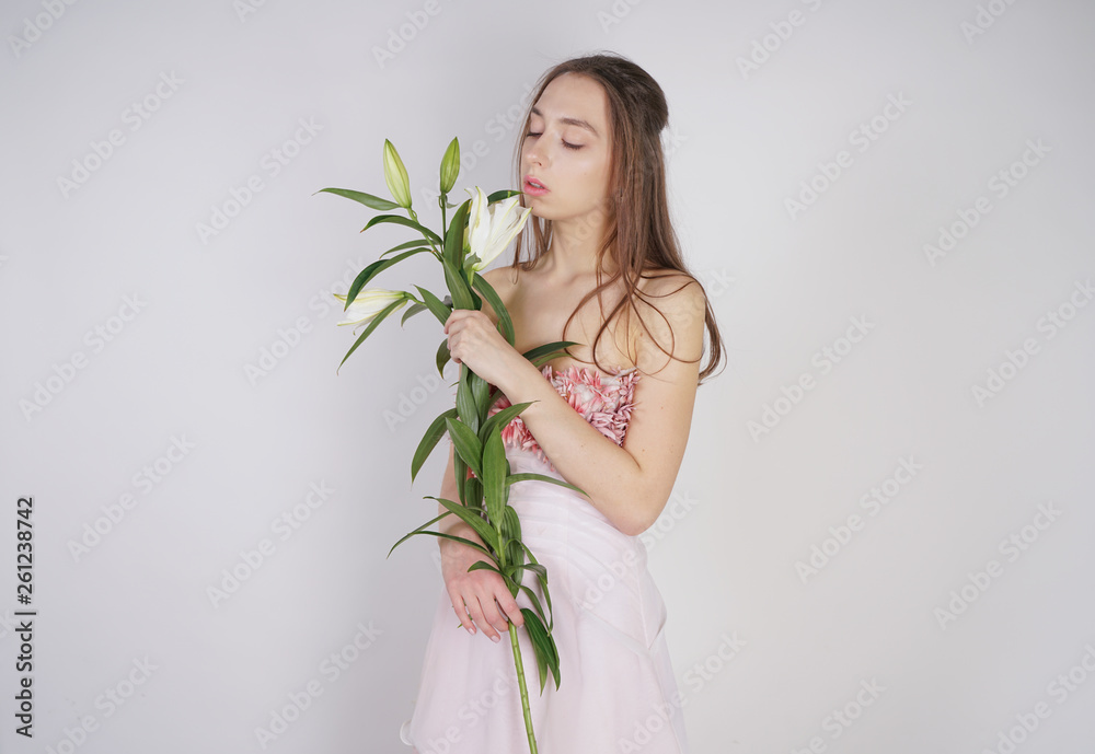 charming young caucasian girl in a pretty dress holds a lush Lily flower in her hands and stands on a white background in the Studio alone charming young caucasian girl in a pretty dress holds a lush Lily flower in her hands and stands on a white background in the Studio alone
