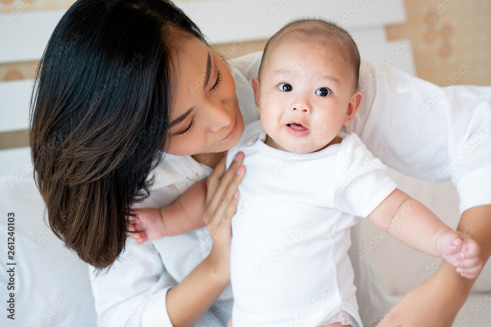 Portrait Mother is taking care of newborn baby wearing clean white clothes In the bedroom. With love in mind to keep children healthy. And cheerful The child has good development. Mother's Day in May