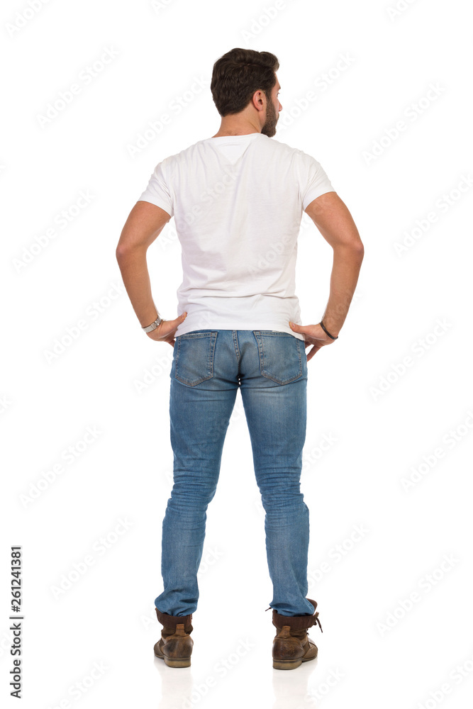Rear View Of Standing Man In Jeans And WhiteT-shirt With Hands On Hip Rear View Of Standing Man In Jeans And WhiteT-shirt With Hands On Hip