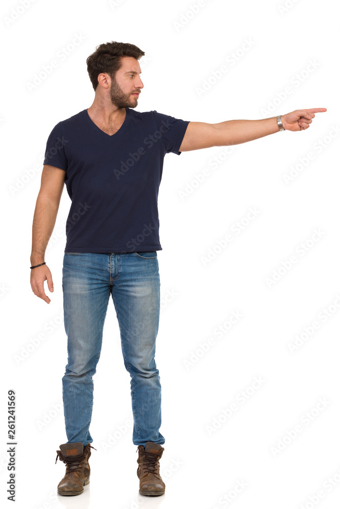 Serious Handsome Man In Jeans T-Shirt And Boots Is Pointing And Looking Away Serious Handsome Man In Jeans T-Shirt And Boots Is Pointing And Looking Away