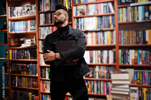 Tall smart arab student man, wear on black jeans jacket and eyeglasses, at library with book at hands.