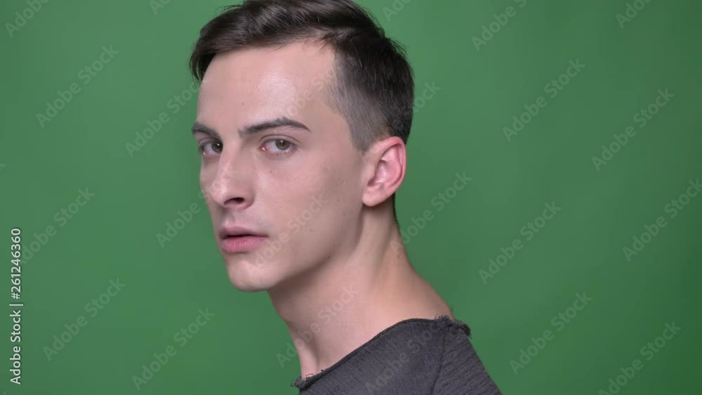 Closeup shoot of young handsome caucasian male face turning and looking straight at camera with background isolated on green Closeup shoot of young handsome caucasian male face turning and looking straight at camera with background isolated on green
