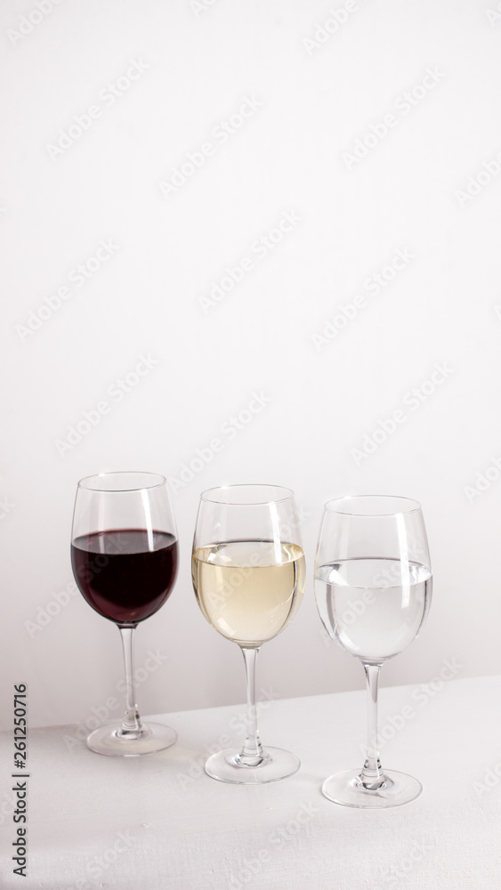Three glasses of red, white wine and water standing in one line on grey background. vertical picture with copy space Three glasses of red, white wine and water standing in one line on grey background. vertical picture with copy space