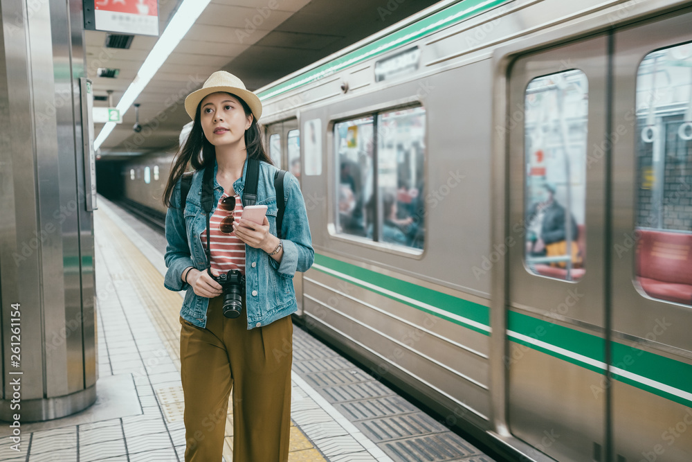 Young woman typing on smart phone at tube station in osaka japan. girl  travel backpacker looking up of road information indicator. beautiful  japanese lady walking on platform and subway train leaving Photos