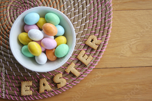 Easter background with colorful chocolate eggs in a bowl with cookies on wooden background
