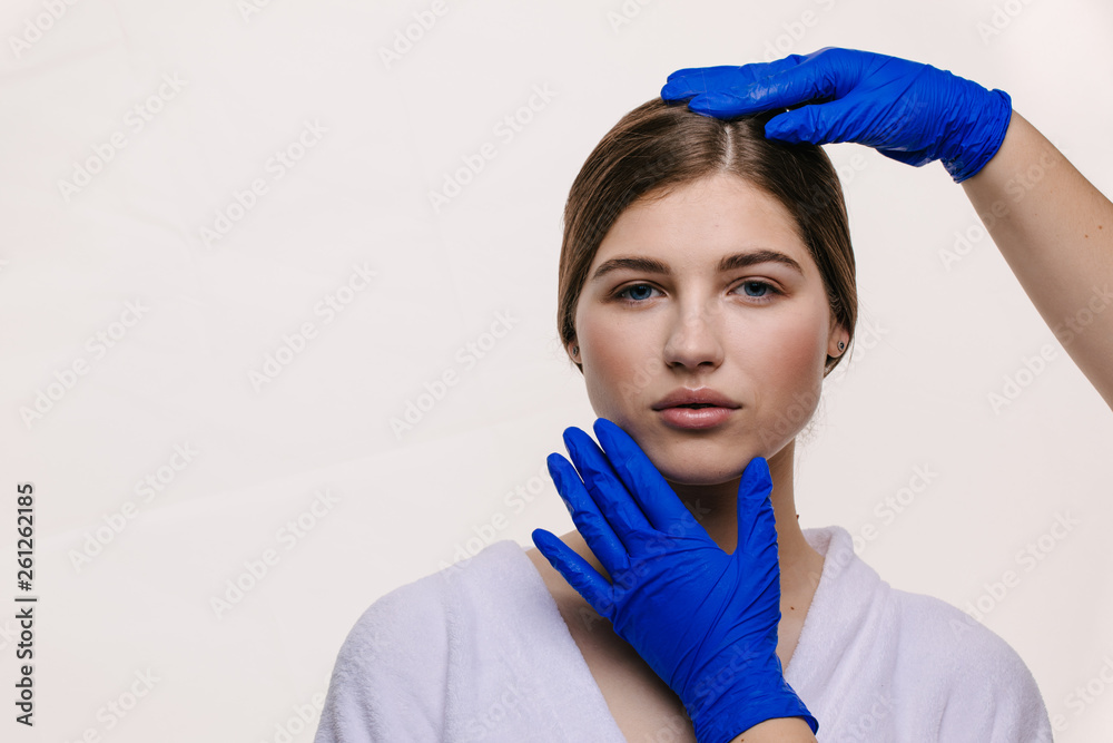 Beauty treatment of the young beautiful female face, doctor's hand in gloves touch face of beautiful young woman isolated on white Beauty treatment of the young beautiful female face, doctor's hand in gloves touch face of beautiful young woman isolated on white