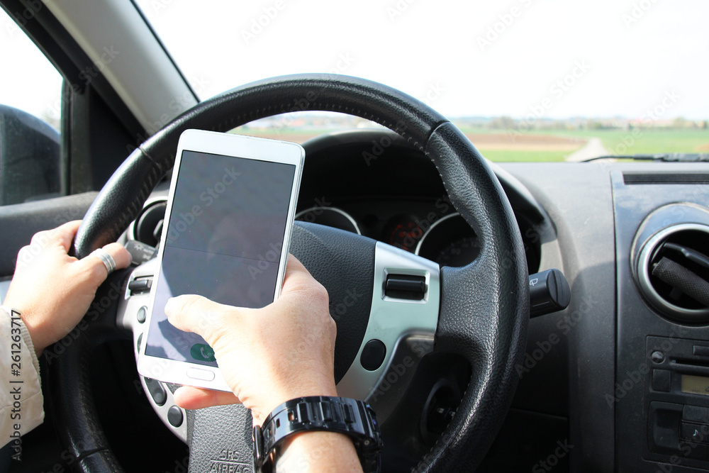 Holding and tipping on a Smart phone while driving a car on the steering wheels Holding and tipping on a Smart phone while driving a car on the steering wheels