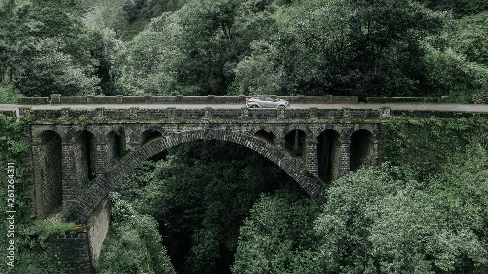 Drone aerial view of a car crossing a stone bridge over a water stream in Cruzinhas, Faial, Madeira island, Portugal.