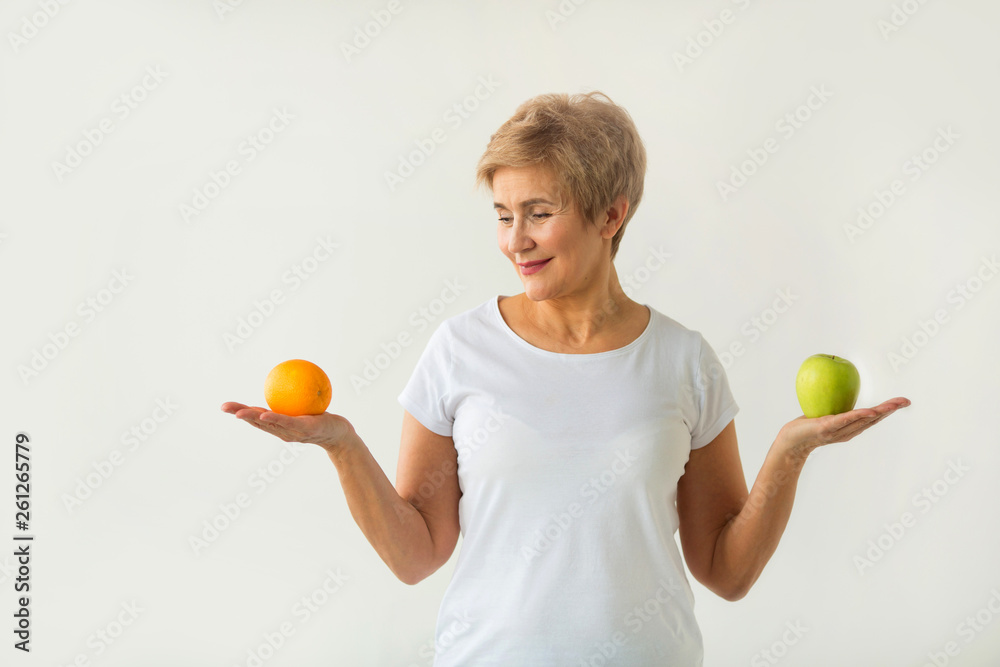 beautiful aged woman with short haircut in a white t-shirt with an apple and an orange on a white background beautiful aged woman with short haircut in a white t-shirt with an apple and an orange on a white background