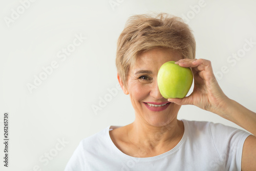 beautiful aged woman with short haircut in a white t-shirt with an apple on a white background © Alexandr