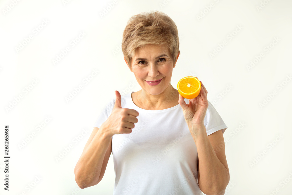 beautiful aged woman with a short haircut in a white T-shirt with oranges in her hands on a white background with a gesture of hand beautiful aged woman with a short haircut in a white T-shirt with oranges in her hands on a white background with a gesture of hand