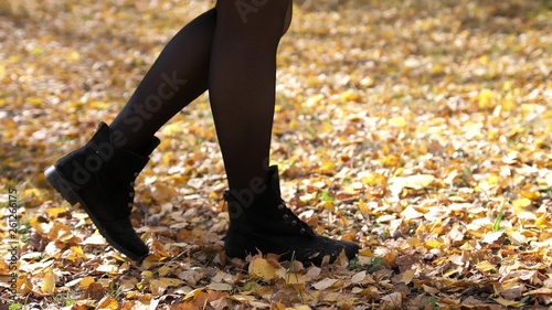 Female steps along the colorful autumn foliage of the city park. Walk in the autumn. Close up legs and shoes view