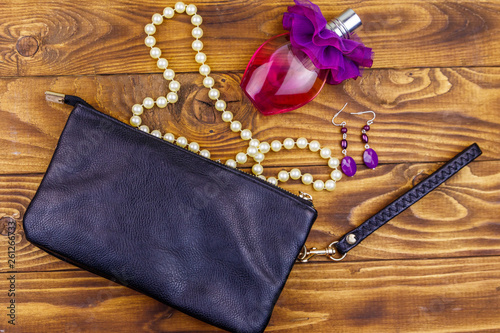 Women accessories on wooden background. Clutch bag, bottle of perfume, pearl necklace and earrings on wood table. Beauty and fashion composition. Top view, flat lay