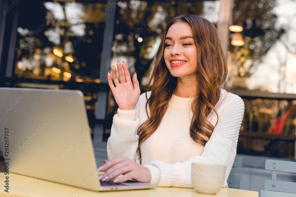 attractive and happy woman waving hand while having video call on laptop attractive and happy woman waving hand while having video call on laptop
